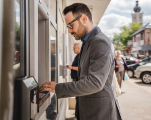 Adult caucasian man stand and hold credit card use cash machine