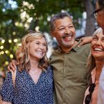 Group of happy senior friends sharing a moment outdoor while embrace. Older men and laughing women chatting together during a walk. Close up face of cheerful retirees enjoying time in a lively city street.