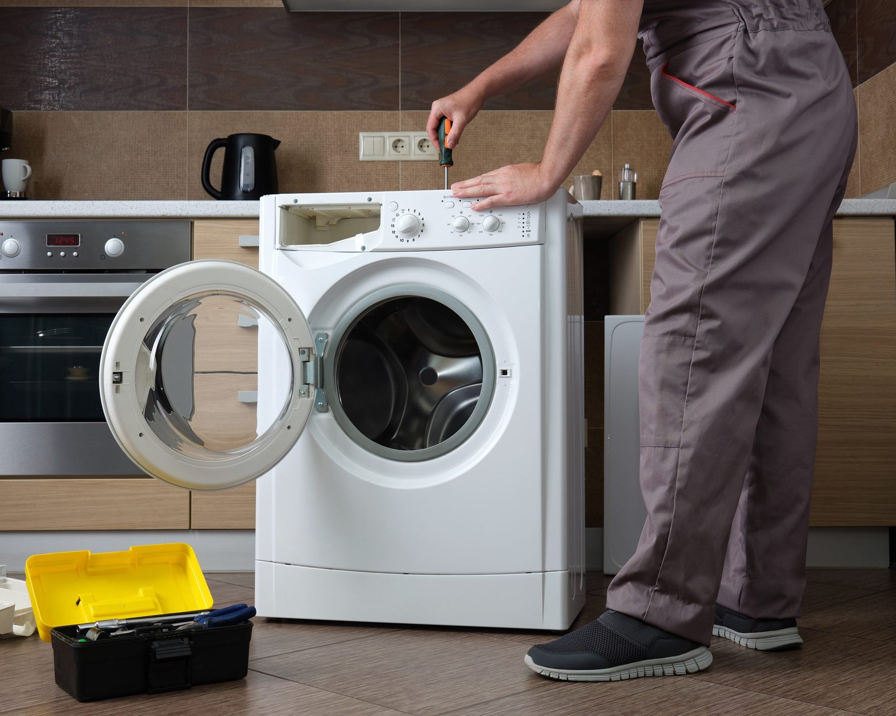 A adult household appliance repairman disassembling a washing machine with a screwdriver. Professional repair of household appliances.